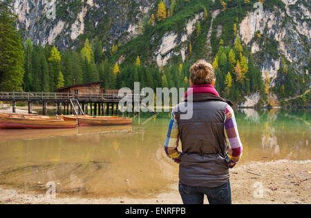 Una bruna donna escursionista, indossando outdoor gear è in piedi a guardare il panorama sul lago di Bries. Barche in legno rustico pier e golden e verdi alberi riflettono l'autunno. Foto Stock