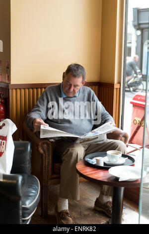 Uomo in coffee shop leggendo un giornale Foto Stock