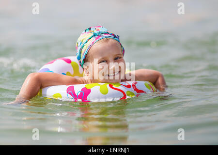 Bambino felice nuota nel mare su anello gonfiabile in una limpida giornata di sole. Profondità di campo. Messa a fuoco selettiva sul modello della fac Foto Stock