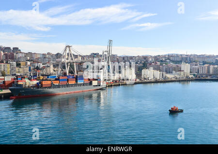 Piccolo rimorchiatore andando verso un contenitore grande nave presso il terminal per container del porto di Vigo, Spagna Foto Stock