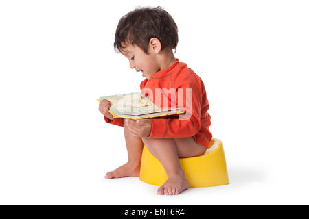 Il Toddler ragazzo seduto su un Vasino e la lettura di un libro su sfondo bianco Foto Stock