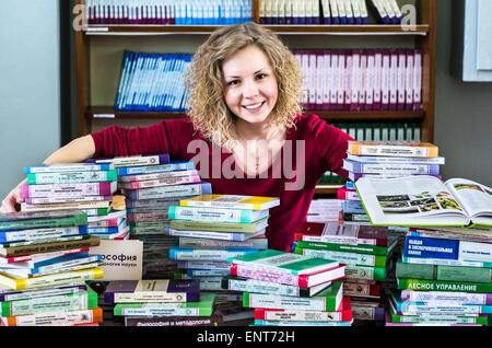 Una ragazza sono trasportano informazioni sulle pile di libri e chiedendo circa i buoni contrassegni Foto Stock