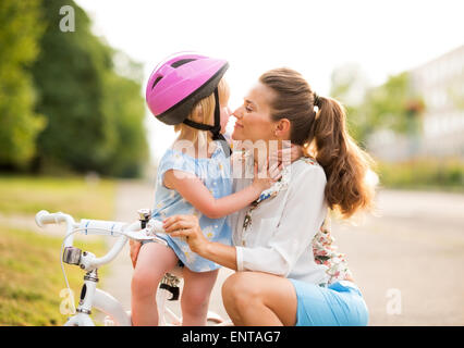 Eschimese baci tra un orgoglioso madre e figlia che ha appena imparato a guidare la sua bicicletta. La madre si inginocchia amorevolmente accanto Foto Stock