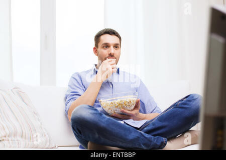 Giovane uomo di guardare la tv e mangiare popcorn a casa Foto Stock
