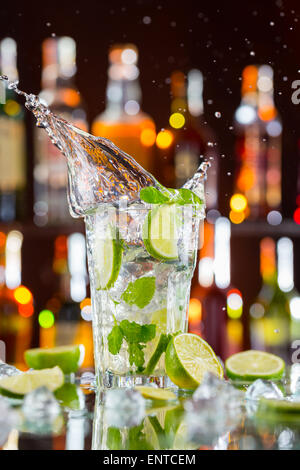 Cocktail Mojito bevanda con splash, servito sul banco bar con bottiglie di sfocatura sullo sfondo Foto Stock