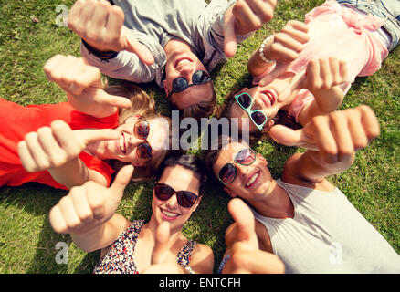 Sorridente amici mostra Thumbs up sdraiati sull'erba Foto Stock