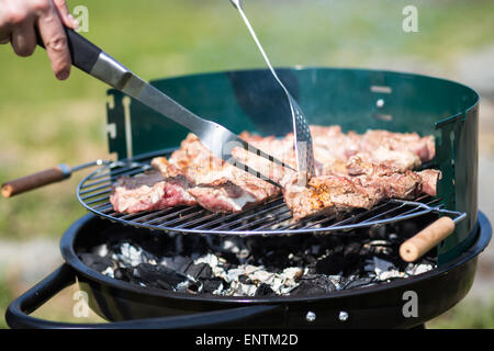 Grigliare carne di maiale sulla brace con strumenti griglia Foto Stock