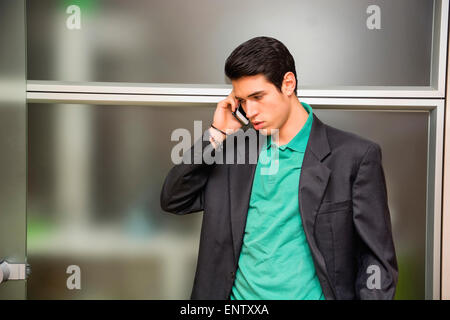 Bel giovane imprenditore nel suo ufficio parlando al cellulare, guardando verso il basso, gravi Foto Stock