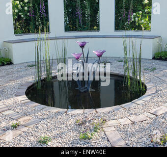 Un piccolo cerchio circolare ghiaia e pietra pavimentata patio - tondo nero riflettente stagno piantato con Horsetail Equisetum arvense scultura in metallo UK Foto Stock