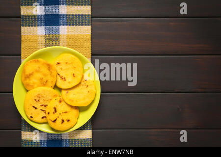 Piastra di arepas fotografato in legno scuro con luce naturale. Arepas sono fatte di colore bianco o giallo di farina di mais (qui giallo) Foto Stock