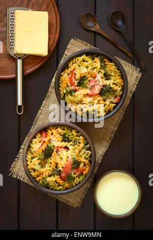 Tricolore al forno fusilli e vegetali (broccoli, pomodoro) casseruola in ciotole rustiche, salsa alla panna, cucchiai, grattugia e formaggio Foto Stock