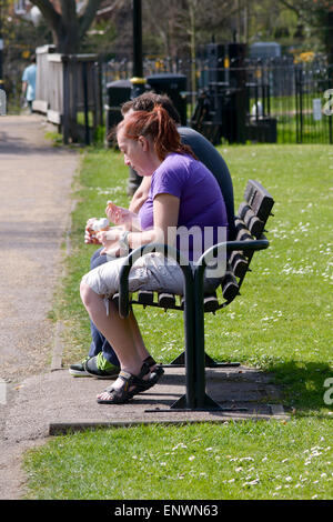 Donna seduto su una panchina nel parco a mangiare il gelato in Bedford, Bedfordshire, Inghilterra Foto Stock