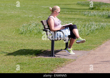 Donna seduto su una panchina nel parco la lettura di libro in Bedford, Bedfordshire, Inghilterra Foto Stock