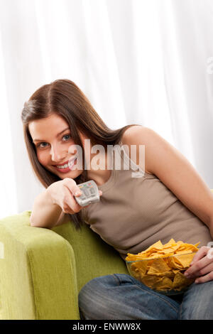 Gli studenti series - sorridente giovane donna guardando la televisione e mangiare patatine Foto Stock