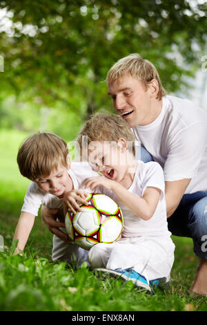 Padre e i due figli di giocare a calcio in un giardino estivo Foto Stock