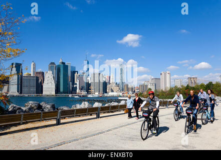 Stati Uniti d'America, New York, il Ponte di Brooklyn Park, gli escursionisti e i ciclisti su un percorso in autunno tra Pier 1 e Pier 2 con la parte inferiore di Manhattan Financial District grattacielo skyline e l'East River oltre. Foto Stock