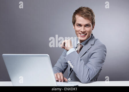 Attraente giovane con un computer portatile su uno sfondo grigio Foto Stock