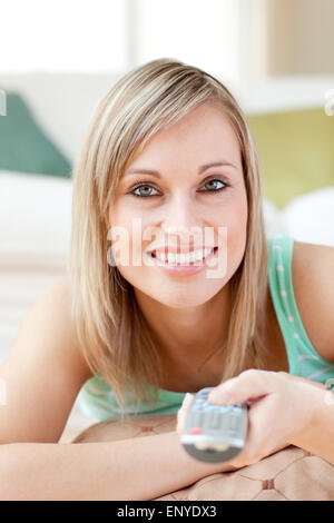 Affascinante donna bionda guardando la TV sdraiato sul pavimento Foto Stock