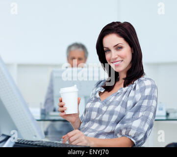 Imprenditrice radiante tenendo un bicchiere alla sua scrivania Foto Stock