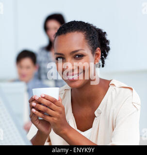 Incandescente imprenditrice di bere un caffè alla sua scrivania Foto Stock