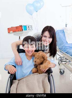 Sorridente piccolo ragazzo seduto su una sedia a rotelle e sua madre Foto Stock