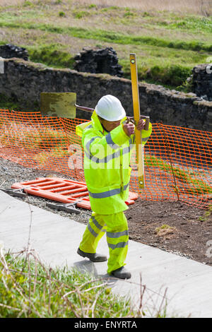 Operatore che trasporta pala e livella a bolla d'aria - operai che gettano un nuovo percorso a Porthgain, Pembrokeshire Coast National Park, Galles, Regno Unito a maggio Foto Stock