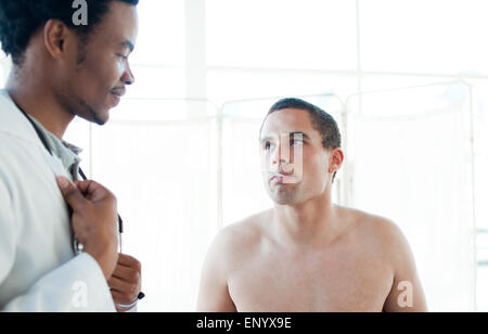 Un medico tenendo il suo paziente la temperatura con un termometro Foto Stock