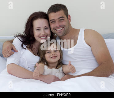 Felice famiglia giovane a letto con il pollice in alto Foto Stock