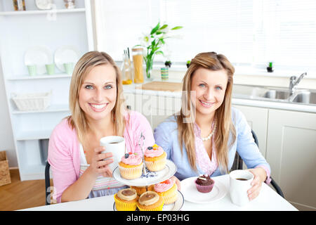 Ritratto di due donne attraenti con tazze di caffè e tortini di seduta in cucina Foto Stock