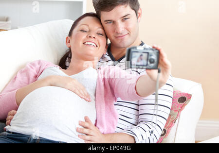 Close-up di una allegra donna incinta e suo marito a scattare foto di loro stessi su un divano Foto Stock