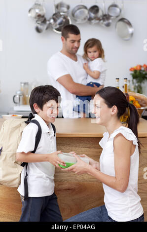 Sorridente madre dando a scuola il pranzo al suo figlio Foto Stock