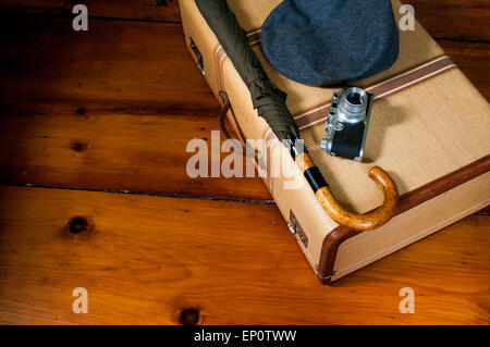 Una valigia vintage, fotocamera, cappello di lana e ombrello sit ordinatamente su un pavimento di legno. Foto Stock