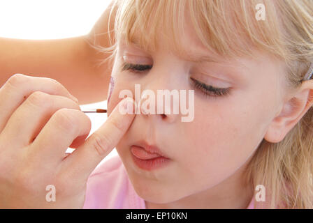 Poco Caucasian ragazza bionda ottenendo il suo volto dipinto. Foto Stock