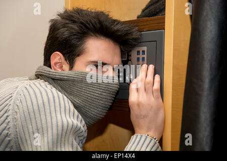 Giovane maschio ladro nasconde il viso con maschera di apertura di una piccola casa di archivio o cassetta di sicurezza Foto Stock