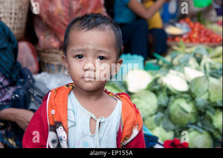 Un piccolo ragazzo in piedi di fronte a verdure fresche in un Rangoon mercato alimentare di Myanmar Foto Stock