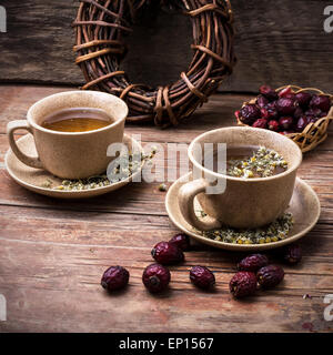 Due tazze di ceramica di infuso di tè con rosa canina e camomilla in mezzo a fasci di radice di liquirizia Foto Stock