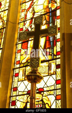 Ottone cristiana altare croce contro una finestra di vetro colorato Foto Stock