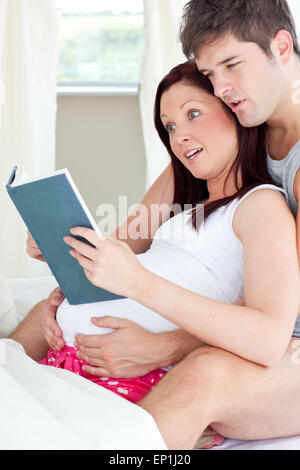 Close-up di un scioccato la donna incinta e il marito a leggere un libro sul divano di casa Foto Stock