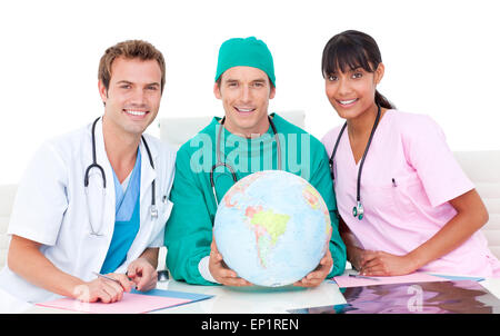 Gioioso team medico guardando il globo terrestre contro uno sfondo bianco Foto Stock
