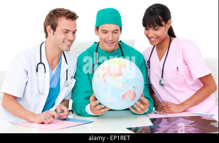 Allegro team medico guardando il globo terrestre contro uno sfondo bianco Foto Stock