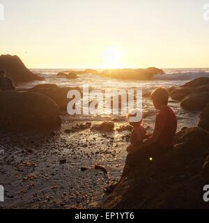 Due ragazzi seduti sulle rocce in spiaggia al tramonto, Dana Point, California, Stati Uniti d'America