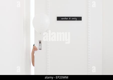 Ragazzo tenendo un palloncino e nascondersi dietro a una porta Foto Stock