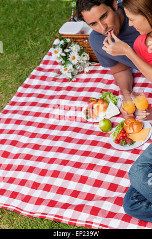 Donna mettendo il cibo in i suoi amici a bocca come essi giacciono su una coperta Foto Stock