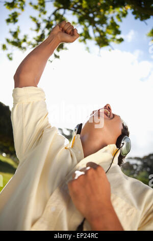 L'uomo alzando il braccio pur utilizzando le cuffie per ascoltare la musica in un parco Foto Stock