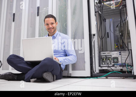 Uomo sorridente seduto sul pavimento i server di controllo con il computer portatile Foto Stock