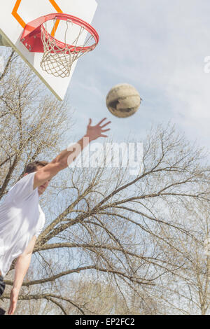 Giovane uomo che fa del basket trick shots come egli salta attraverso l'aria Foto Stock