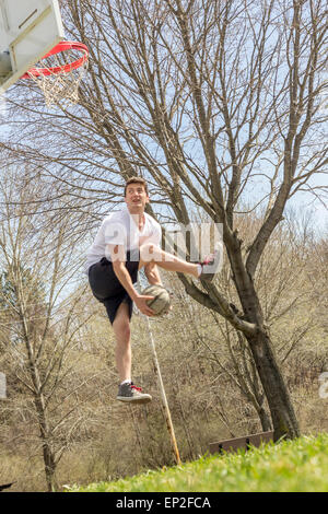 Giovane uomo che fa del basket trick shots come egli salta attraverso l'aria Foto Stock