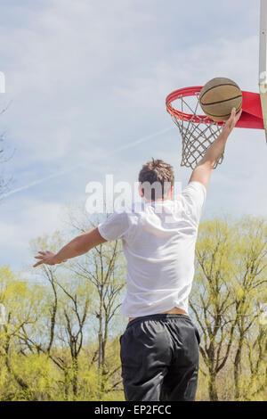 Giovane uomo che fa del basket trick shots come egli salta attraverso l'aria Foto Stock