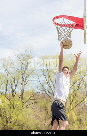 Giovane uomo che fa del basket trick shots come egli salta attraverso l'aria Foto Stock