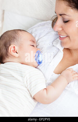 Ritratto di un simpatico baby dormendo pacificamente nelle braccia della madre che giace nel divano Foto Stock